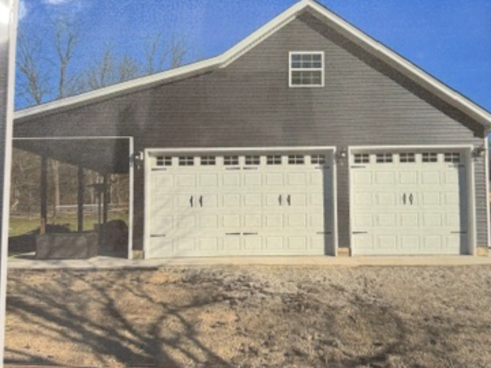 Three-car garage with cream doors, gray siding, and covered carport on left side
