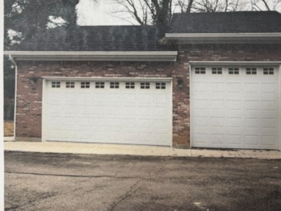 Two white garage doors on a brick house with driveway