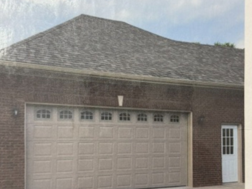 Brick garage with gray shingled roof and white paneled garage door