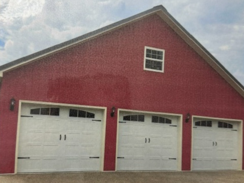 Red barn with three white garage doors and small windows