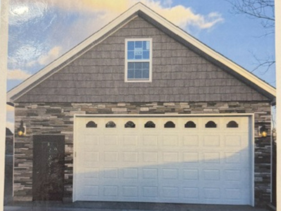 Single-car garage with white door, dark brick siding, and gabled roof with attic window